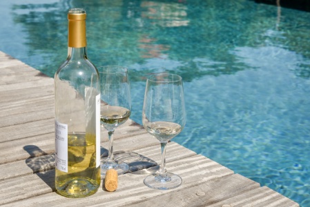 fles witte wijn en twee glazen naast het zwembad