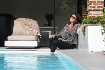 vrouw zit met een drankje op de rand van een zwembad in een stadstuin met een ultiem vakantie gevoel