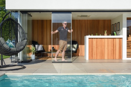 man doet ramen open van poolhouse naast wit zwembad met maatwerk hoektrap