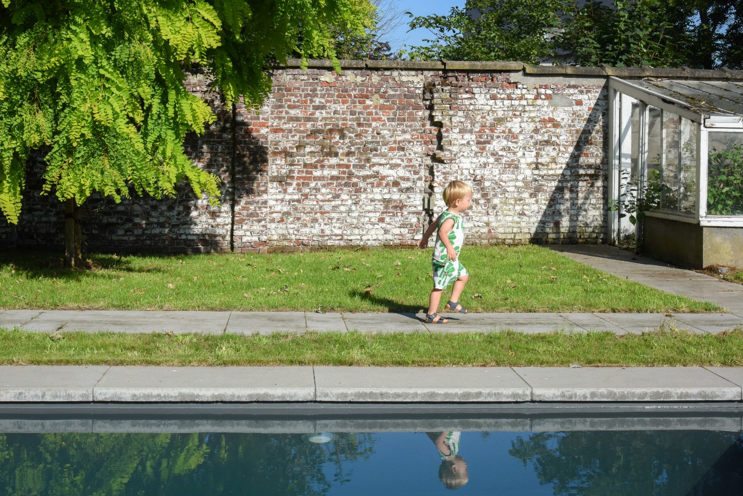 kind loopt naast een bio zwembad of biopool in een parktuin 