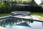 loungezetel met zonnewering op het terras naast een bio zwembad of biopool in een parktuin 
