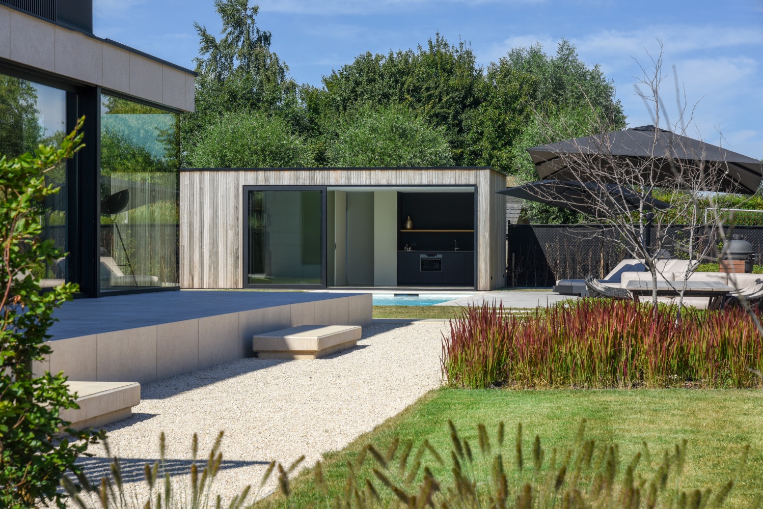 tuin en poolhouse naast een strak wit zwembad bij moderne villa