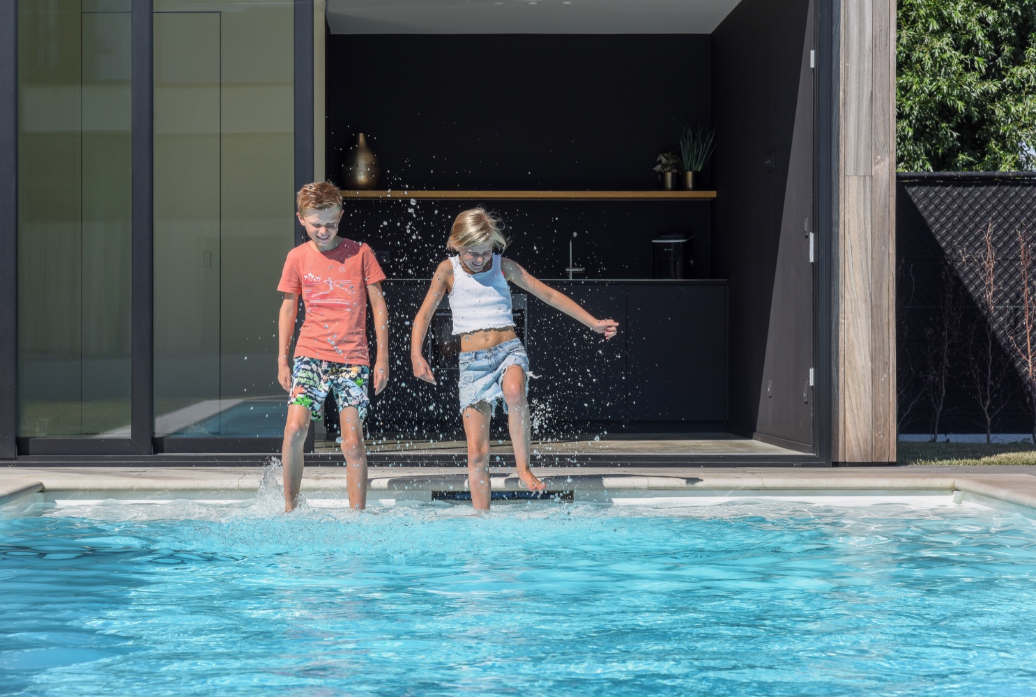 kindjes spelen naast een strak wit zwembad bij moderne villa