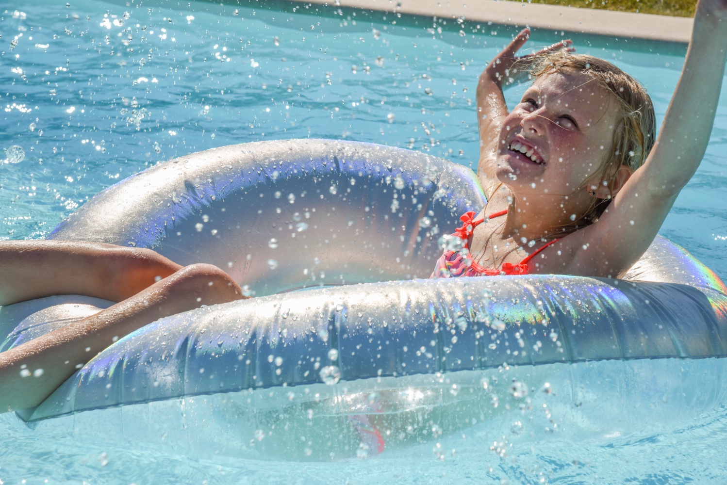 kind speelt in het water van een strak wit zwembad bij moderne villa