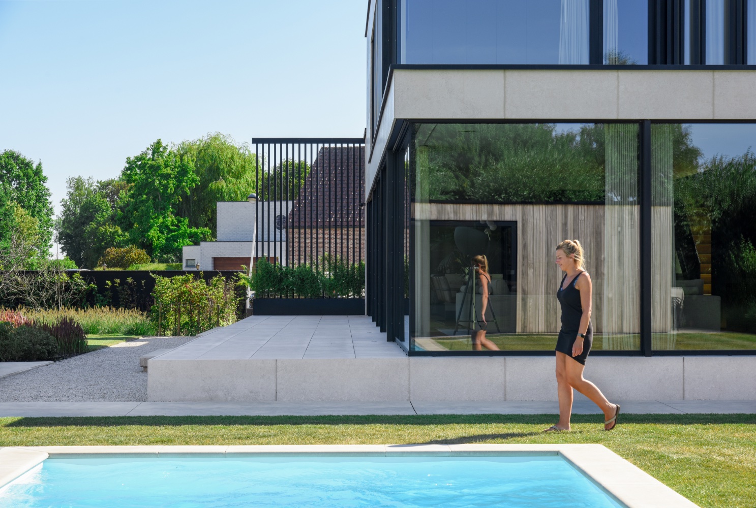 vrouw loopt naast strak wit zwembad bij moderne villa